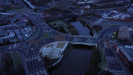 Aerial-view-looking-down-city-centre-canal-roundabout-infrastructure-suburban-streets-traffic-at-daybreak-slow-dolly-left
