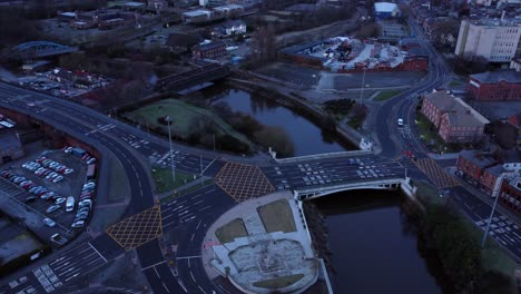 Aerial-view-looking-down-city-centre-canal-roundabout-infrastructure-suburban-streets-traffic-at-daybreak-slow-left-orbit-shot
