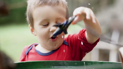 Young-caucasian-boy-pulling-plastic-toy-airplane-out-of-barrel-full-of-water,-SLOW-MOTION