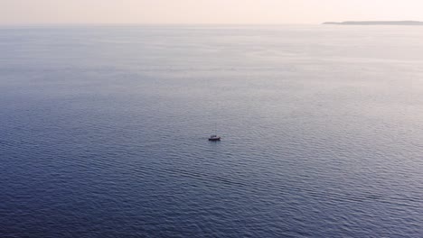 Lonely-boat-traveling-across-the-calm-sea-waters-during-the-foggy-sunset