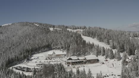 Kope-ski-resort-in-the-Pohorje-mountains-with-parking-and-visitors-exploring,-Aerial-pan-right-shot