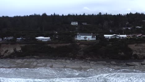 Cliffside-view-of-houses,-Seal-Rock-in-Oregon-Coast,-dark-afternoon,-wave-from-Ocean-shore,-aerial-pan-view