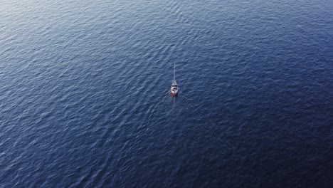 Sailboat-travelling-through-blue-ocean-waters,-rising-aerial-tilt-view