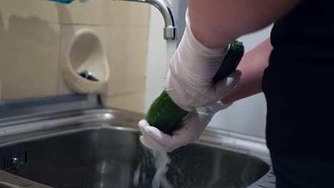A-cucumber-is-washed-under-running-water-with-disposable-gloves
