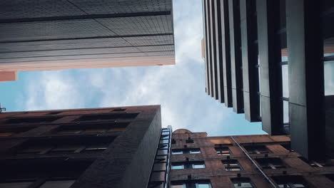 Looking-Up-Between-Tall-Buildings-To-The-Blue-Sky-Above-In-The-City---low-angle-shot