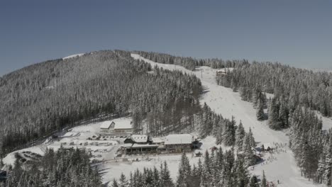 Kope-ski-resort-in-Slovenia-at-the-Pohorje-mountains-with-people-skiing-down-the-Ribnica-One-track,-Aerial-pan-right-shot