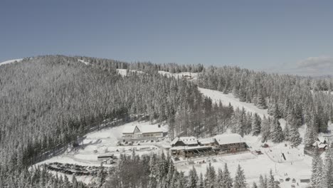 Kope-ski-resort-and-hotel-n-the-Pohorje-mountains-with-visitors-on-the-snowed-track,-Aerial-pan-right-shot