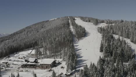 Kope-ski-resort-Ribnica-One-track-with-descending-skiers-and-snowboarders,-Aerial-approach-shot
