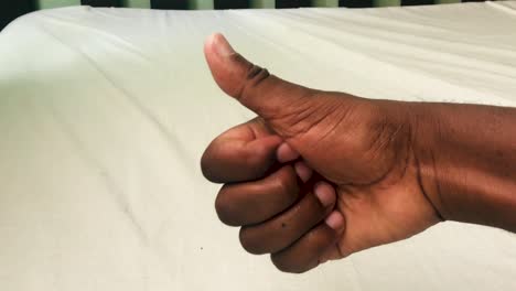 Thumbs-up-of-a-black-right-hand-over-the-wooden-bed-with-white-bedcover