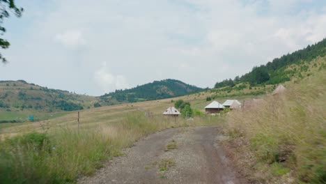 Road-through-the-mountain-leading-to-small-village-wooden-houses-on-the-green-field