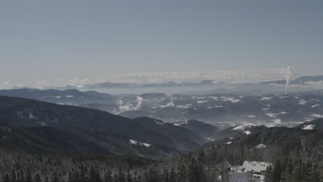 Kope-winter-resort-RV-and-car-parking-lot-in-the-Pohorje-mountains-with-smoke-in-the-distance,-Aerial-tilt-up-reveal-shot