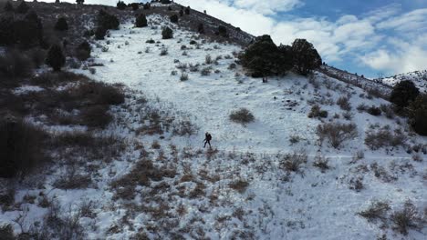 Aerial-View-of-Solo-Hiker-Walking-on-Snow-Capped-Hillside