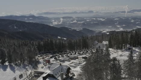 Kope-ski-resort-complex-RV-and-car-parking-in-the-Pohorje-mountains-with-smoke-in-the-distance,-Aerial-dolly-in-reveal-shot