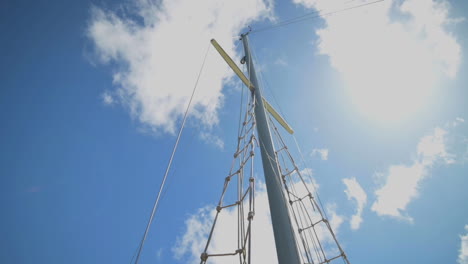 A-Sail-Boat-Mast-Against-Beautiful-Blue-Sky-With-Clouds---low-angle-shot