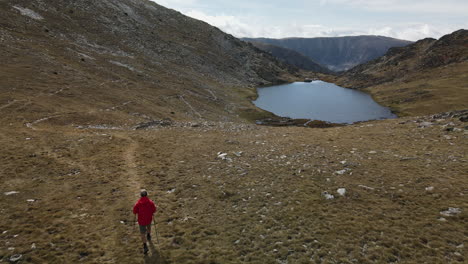 Man-on-a-red-coat-walking-on-the-mountains-arriving-to-a-beautiful-little-lake-in-Puymorens