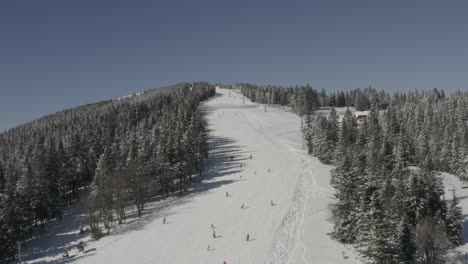 Kope-ski-resort-Slovenia-with-skiers-going-downhill-at-Ribnica-One-track,-Aerial-approach-shot