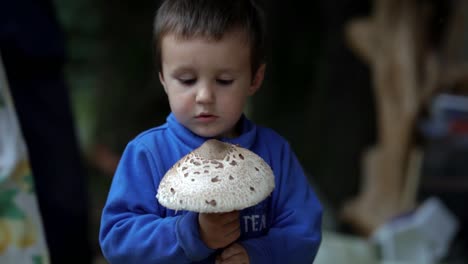 A-little-caucasian-boy-rotates-his-head-while-holding-a-huge-flat-mushroom,-SLOW-MOTION