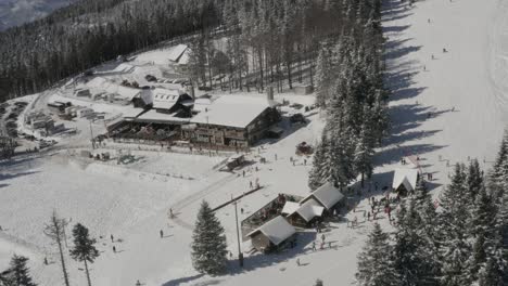 Kope-ski-resort-in-the-Pohorje-mountains-with-visitors-on-the-snowed-track-and-sledding,-Aerial-pan-right-shot