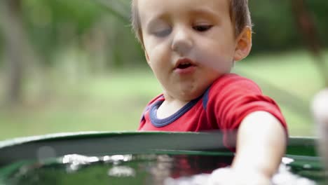 Little-caucasian-boy-playing-with-plastic-air-plane-toy-in-a-barrel-filled-with-water,-SLOW-MOTION