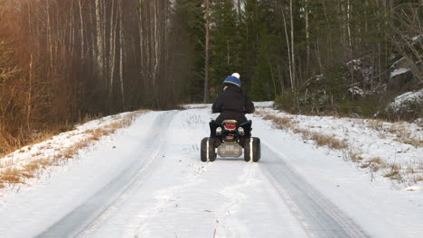 Little-Kid-drives-Quad-Bike-on-deserted-road-in-cold-winter-forest-in-Northern-Finland