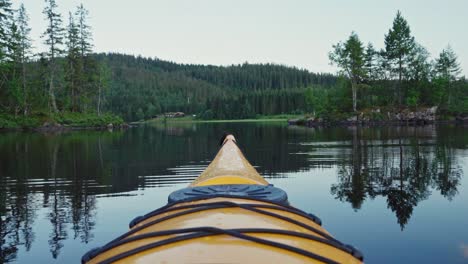 Tip-Of-Yellow-Kayak-Floating-In-Lake-With-Forested-Mountain-In-Background-In-Norway