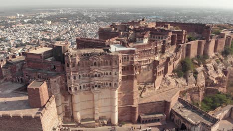 Aerial-drone-footage-tilting-down-a-large-palace-on-top-of-a-hill-above-the-vast-city-of-Jodhpur,-India