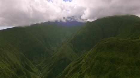 Thick-shiny-clouds-covering-green-mountains-peak,-soft-sunlight,-aerial-view