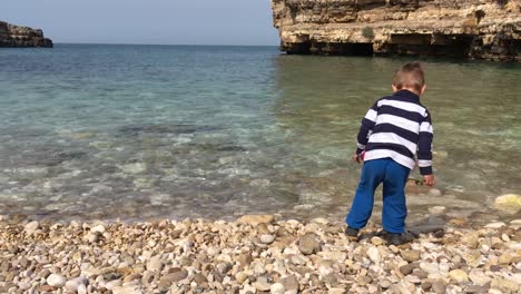 Small-boy-on-the-beach-throwing-rock-into-sea-water,-child-vacation-at-seaside