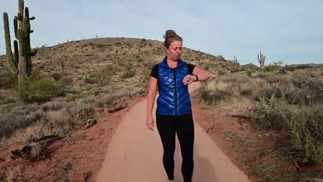 Woman-walking-and-checking-smart-watch-on-paved-desert-trail