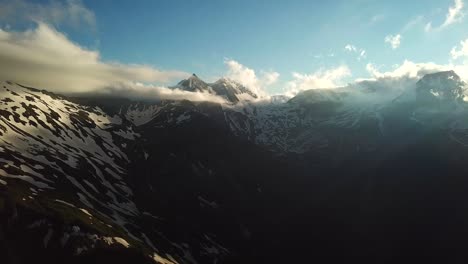 Vista-Aérea-Del-Paisaje-De-Los-Rayos-Del-Sol-A-Través-De-Un-Paisaje-Nuboso-Sobre-Las-Montañas-Austriacas-Picos-Nevados