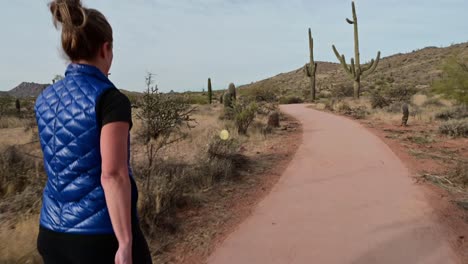 Mujer-Con-Chaleco-Azul-Caminando-Por-Un-Sendero-Pavimentado-En-El-Desierto