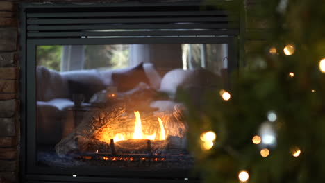 Sliding-View-of-a-Cozy-Fire-in-the-Fireplace-With-a-Christmas-Tree-in-the-Foreground---slow-motion