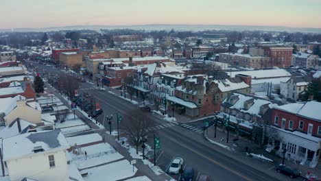 Aerial-establishing-shot-of-Main-Street,-Small-Town-America,-storefronts-and-colonial-homes-in-United-States-historic-town-during-winter-snow