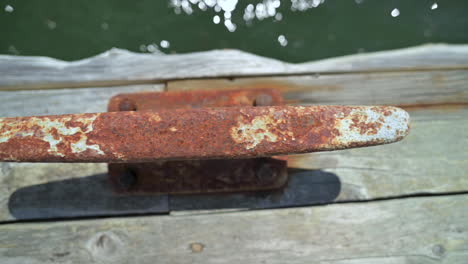 Old-Metal-Cleat-On-Wooden-Dock-To-Tie-Boats-Up---close-up,-slider-right