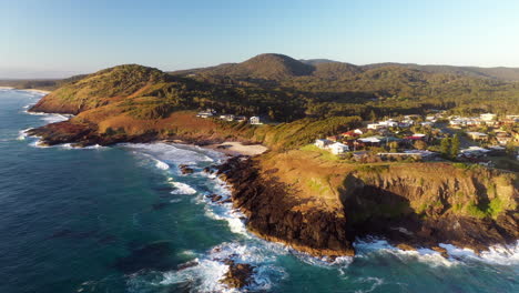 Wide-rotating-drone-shot-of-rocky-coastline-at-Scotts-Head-beach-and-town-in-Australia
