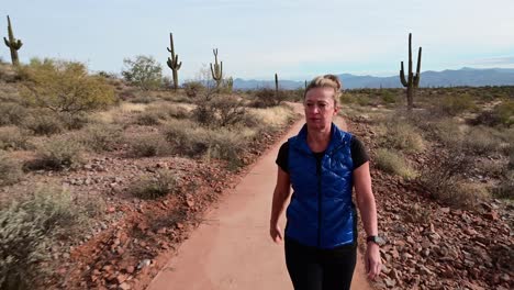 Woman-walking-on-paved-trail-in-desert-landscape