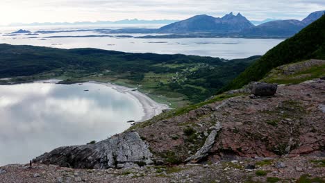 Hombre-Caminando-En-La-Cima-De-Una-Montaña-Rocosa-Con-Vistas-Al-Hermoso-Lago-En-Noruega,-Drone-Aéreo