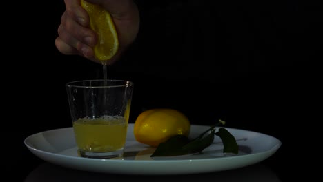 Hand-squeezing-sliced-yellow-lemon-into-glass,-fresh-juice-of-citrus-with-vitamins