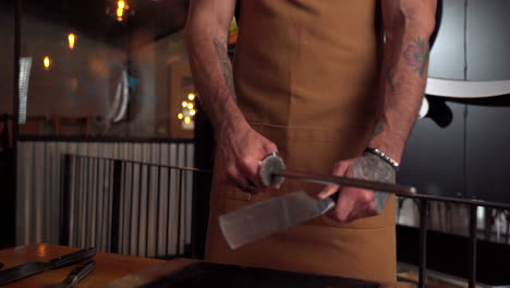 Male-tattooed-latin-model-sharpen-barbecue-butcher-knife-slider-shot-slot-motion