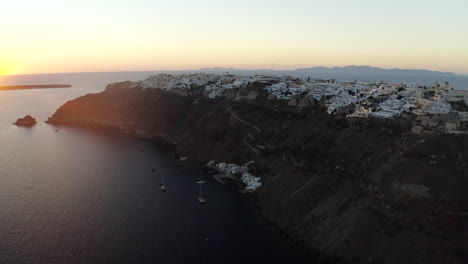 Oia-Santorini-island-sunset-drone-shot-overlooking-white-buildings-and-the-sea,-Greece-in-4K