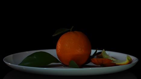 Orange-with-leaves-and-peels-falling-into-plate,-fresh-juicy-citrus-for-fruit-salad