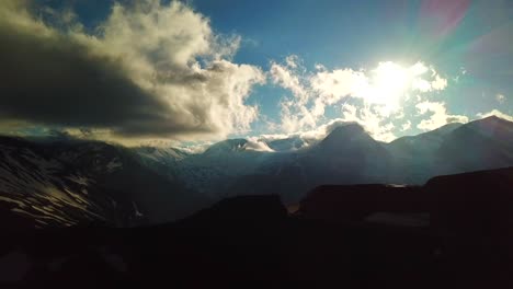 Aerial-view-of-sun-rays-through-a-cloudscape-over-austrian-mountains-snowy-summit