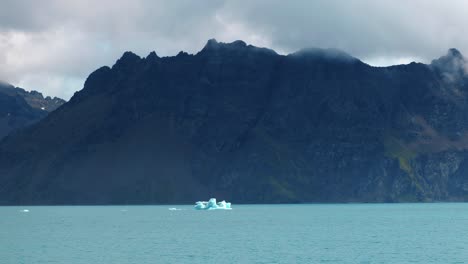 Small-iceberg-in-front-of-a-huge-mountain-range-on-a-sunny-day-in-turquoise-water