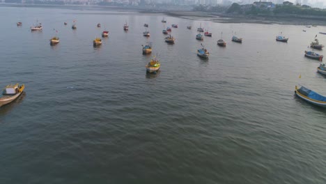 Flying-over-the-fishermen's-boats-parked-at-the-Koliwada-next-to-Worli-Fort,-revealing-the-Mumbai-Cityscape-view-of-skyscrapers-in-the-back-with-settlements-to-contrast