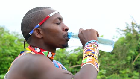 Masai-Mann-Trinkt-Wasser-Aus-Einer-Plastikflasche,-Während-Er-Eine-Traditionelle-Massai-Kleidung-Trägt