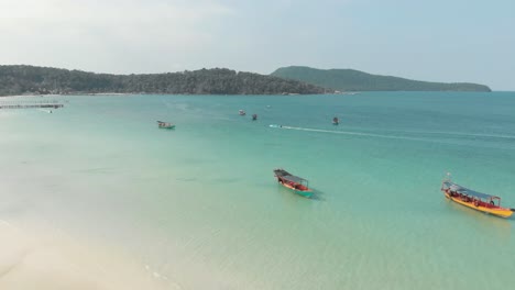 Shallow-Paradisiac-waters-of-Saracen-Bay-populated-by-wooden-fishing-boats,-locals-and-tourists-in-Koh-Rong-Sanloem,-Cambodia---Aerial-Low-angle-fly-over