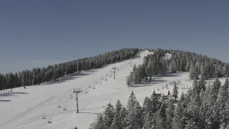 Ski-lift-and-main-downhill-track-at-Kope-ski-resort-Slovenia,-Aerial-orbit-left-reveal-shot