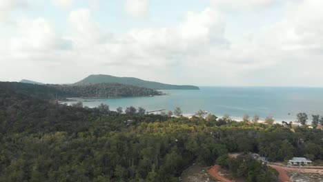 Exotic-green-lush-hills-that-meet-the-turquoise-sea-in-Saracen-Bay-in-Koh-Rong-Sanloem,-Cambodia---Aerial-wide-low-angle-shot