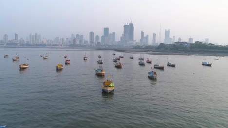 Flying-over-the-fishermen's-boats-parked-at-the-Koliwada-next-to-Worli-Fort,-revealing-the-Mumbai-Cityscape-view-of-skyscrapers-in-the-back-with-settlements-to-contrast