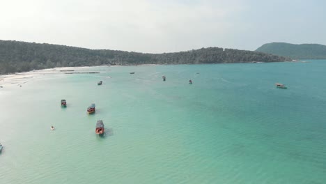 Cambodian-wooden-rural-fishing-boats-resting-on-the-turquoise-exotic-Saracen-Bay-in-Koh-Rong-Sanloem,-Cambodia---Aerial-Panoramic-shot